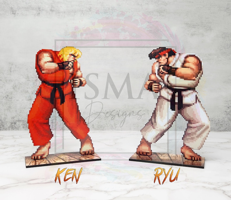 May include: Two pixel art figures of video game characters, Ken and Ryu, from the Street Fighter series. Ken is wearing a red gi with a black belt and Ryu is wearing a white gi with a black belt. Both figures are in a fighting stance.