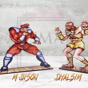 May include: Two pixel art figures from the Street Fighter video game series. The figures are standing on wooden bases. The figure on the left is M. Bison, a red and white character with a black hat. The figure on the right is Dhalsim, a yellow and brown character with a red headband.