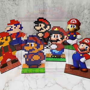 Peut inclure: Plusieurs figurines sur le thème de Mario. Les figurines comprennent des versions pixelisées et 3D de Mario, chacune étant posée sur un socle. La palette de couleurs comprend le rouge, le bleu, le marron et le vert, avec des détails de briques et d'herbe sur les socles.