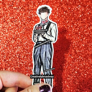 May include: A sticker featuring a watercolor illustration of a person in a white shirt, suspenders, and gray pants, holding a bouquet. The sticker has the text "Creativelybroadway" on it. The background is a sparkly red.