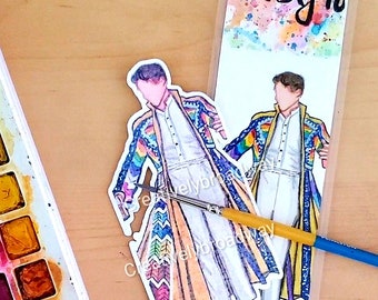 May include: A bookmark featuring the name "Joseph" in black script over a watercolour splash. Two illustrations of a person in a colourful coat and white outfit are shown. A watercolour paint set and paintbrush are also visible.