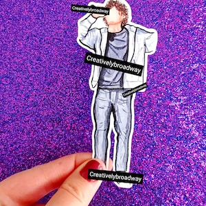 May include: A sticker with a watercolour illustration of a person in a white jacket, grey shirt, and jeans. The text "Creativelybroadway" is printed on the sticker in several places.