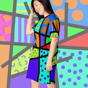 May include: A woman wearing a colourful geometric print dress with short sleeves. The dress features a variety of shapes and colours, including blue, green, orange, and purple.