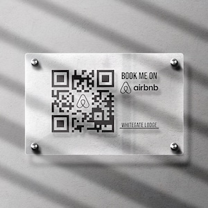 May include: Transparent acrylic sign featuring a QR code, the Airbnb logo, and the text "BOOK ME ON airbnb" and "WHITEGATE LODGE". The sign is fixed to a grey wall with silver fixings.