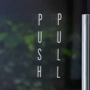 May include: A glass door with the word "PUSH" written in white letters on it. The letters are slightly blurred.
