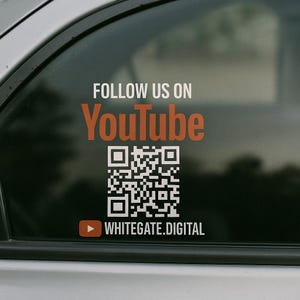 May include: A white sticker on a car window with the text "FOLLOW US ON YouTube" in orange and white. A black and white QR code is below the text, and the text "WHITEGATE.DIGITAL" is below the QR code with a red play button icon.