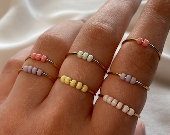 Sencillos anillos dorados antiestrés con coloridas cuentas de vidrio en tonos pastel.