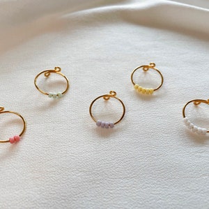May include: Five gold rings with different colored beads. The rings are all the same size and shape. The beads are in a variety of colors, including pink, white, light green, and light purple.