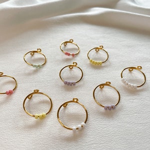 May include: A set of ten gold rings with colorful beads. Each ring has a different color of beads, including pink, yellow, white, and purple.