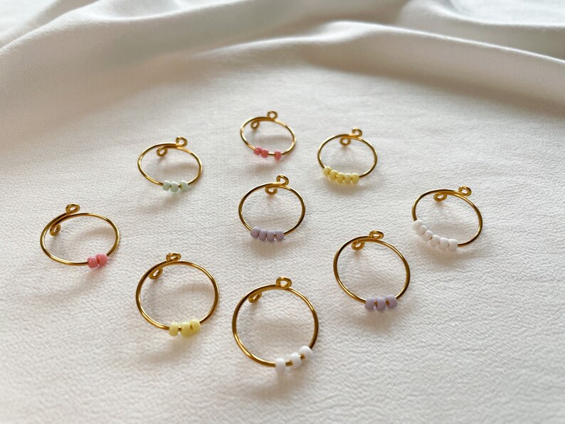 May include: A set of ten gold rings with colorful beads. Each ring has a different color of beads, including pink, yellow, white, and purple.