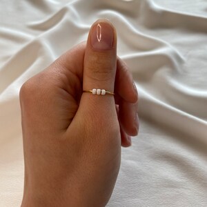 May include: A gold ring with three white beads on a thumb.