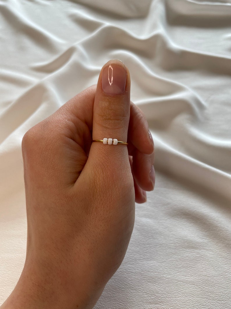 May include: A gold ring with three white beads on a thumb.