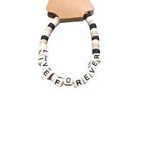 May include: A handmade bracelet with the words "LIVE FOREVER" spelled out in white letter beads. The bracelet features a mix of black, white, and gray disc-shaped beads. The bracelet is attached to a brown tag that reads "Handmade with love."