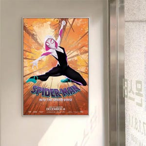 May include: A framed movie poster for "Spider-Man: Into the Spider-Verse." The poster shows Spider-Gwen in a black and white suit with pink accents, leaping against a backdrop of orange and brown trees. The movie title is prominently displayed in a stylized font.