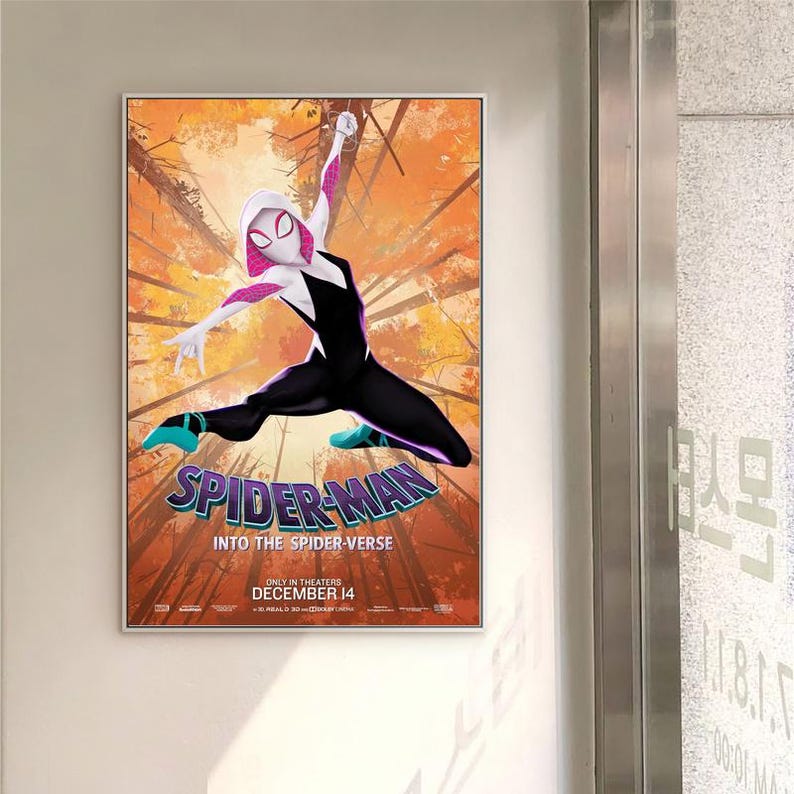 May include: A framed movie poster for "Spider-Man: Into the Spider-Verse." The poster shows Spider-Gwen in a black and white suit with pink accents, leaping against a backdrop of orange and brown trees. The movie title is prominently displayed in a stylized font.