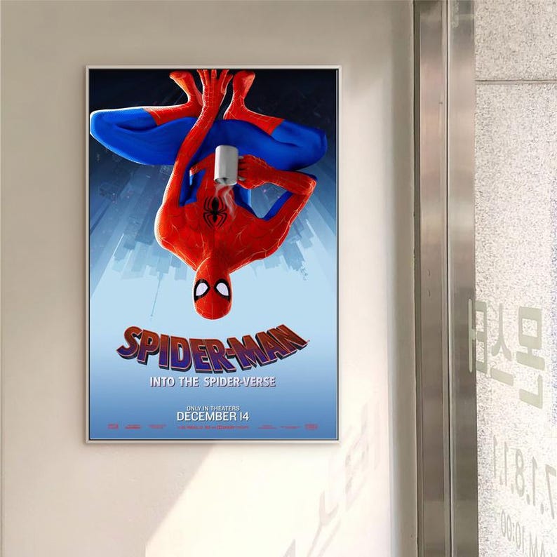 May include: A framed movie poster for "Spider-Man: Into the Spider-Verse" showing the superhero upside down, holding a mug. The poster has a blue background with the movie title in a stylized font and the release date, December 14.