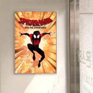 May include: Framed poster of Spider-Man from "Into the Spider-Verse." The image shows Spider-Man in a dynamic pose against an orange and brown forest background. The title "Spider-Man" is displayed in red. The poster is in a white frame.