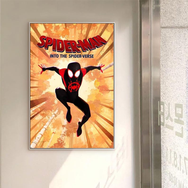 May include: Framed poster of Spider-Man from "Into the Spider-Verse." The image shows Spider-Man in a dynamic pose against an orange and brown forest background. The title "Spider-Man" is displayed in red. The poster is in a white frame.