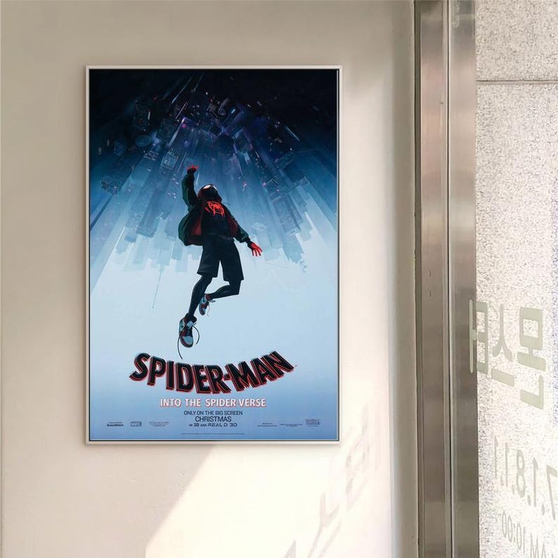 May include: A framed poster for the film "Spider-Man: Into the Spider-Verse." The image shows Spider-Man in a dynamic pose, set against a backdrop of a city skyline. The poster is in a white frame, with the film's title clearly visible.