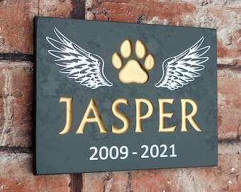 May include: A black slate plaque with a gold paw print and white wings. The plaque reads "JASPER 2009-2021".