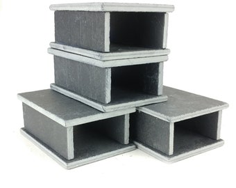 May include: Four stacked black slate coasters with a rectangular shape and a cut-out design. Each coaster has a light gray border.