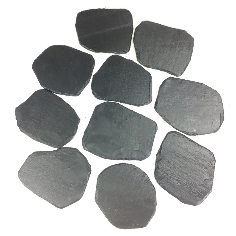 May include: A collection of ten irregularly shaped, dark gray slate coasters. Each coaster has a rough, textured surface and varying dimensions. The coasters are arranged on a white background, showcasing their natural stone appearance.