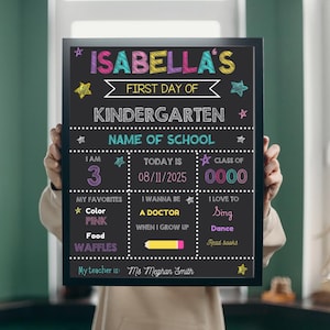 以下が含まれることがあります： 「Isabella's First Day of Kindergarten」と書かれたカラフルな文字が入った黒いフレームの黒板。年齢、学校名、お気に入りなど、個人の詳細を入力できるスペースがあります。黒板は人が持っています。