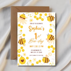 May include: A birthday invitation with a bee theme. The invitation features the text "Sophia's 1st Bee-day" with illustrations of bees, flowers, and a honeycomb. The invitation is on a white background with a brown envelope.