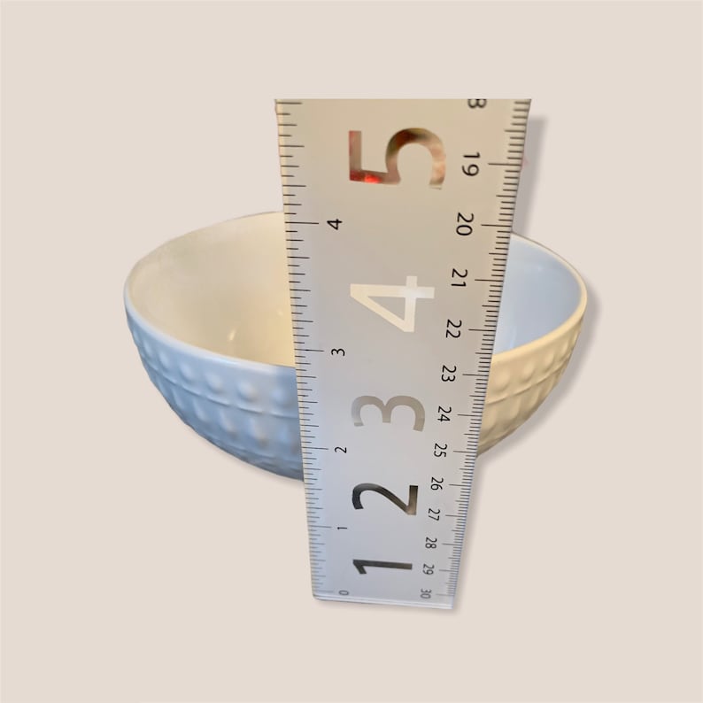 May include: A white ceramic bowl with a textured pattern, measured with a ruler to be approximately 5 inches in diameter.