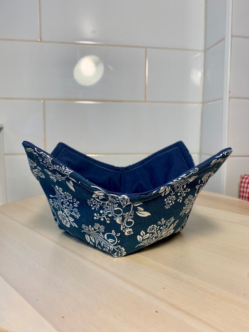 May include: A blue fabric bowl with a white floral pattern. The bowl is folded and sitting on a wooden surface.