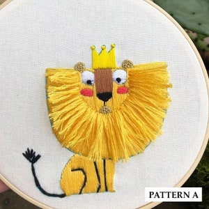 May include: Embroidered lion with a yellow mane and a gold crown, sitting on a white background. The lion has a brown nose, black eyes, and pink cheeks. The text "PATTERN A" is in the bottom right corner.