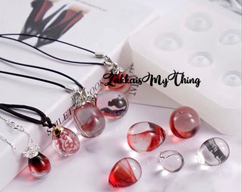 May include: A collection of handmade resin pendants and beads. The pendants are on black cords and silver chains. The resin pieces are clear with red and black accents. The text "Zakkais My Thing" is visible.