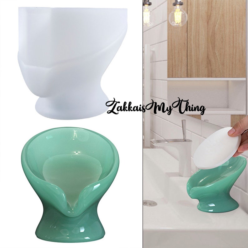May include: A white and a teal soap dish with a curved design. The teal dish holds a white bar of soap. The soap dishes have a unique, modern shape, and are displayed on a white surface.