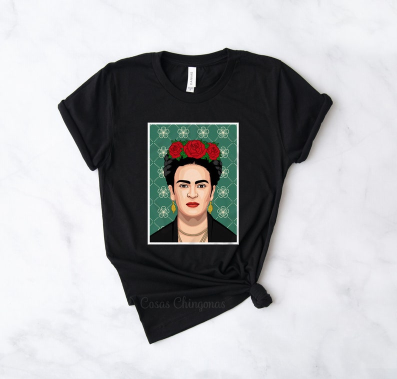 Puede incluir: Camiseta negra con un estampado gr&aacute;fico de Frida Kahlo con una corona de flores. El fondo es verde con un patr&oacute;n geom&eacute;trico. El texto "Casas Chingonas" est&aacute; impreso en la parte inferior de la camiseta.