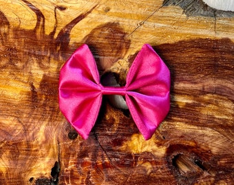 Peut inclure: Un nœud papillon en satin fuchsia vif, noué au centre, avec des boucles symétriques. Le nœud est posé sur un fond en bois naturel texturé, mettant en valeur sa couleur vive et son design élégant. Idéal pour les accessoires de cheveux ou les cadeaux.