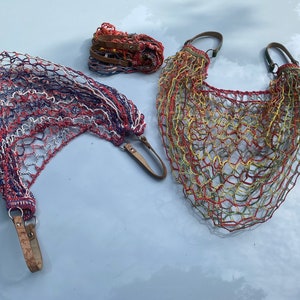 May include: Two crocheted string bags with leather handles. One bag is red, white, and blue. The other bag is green, yellow, and red.
