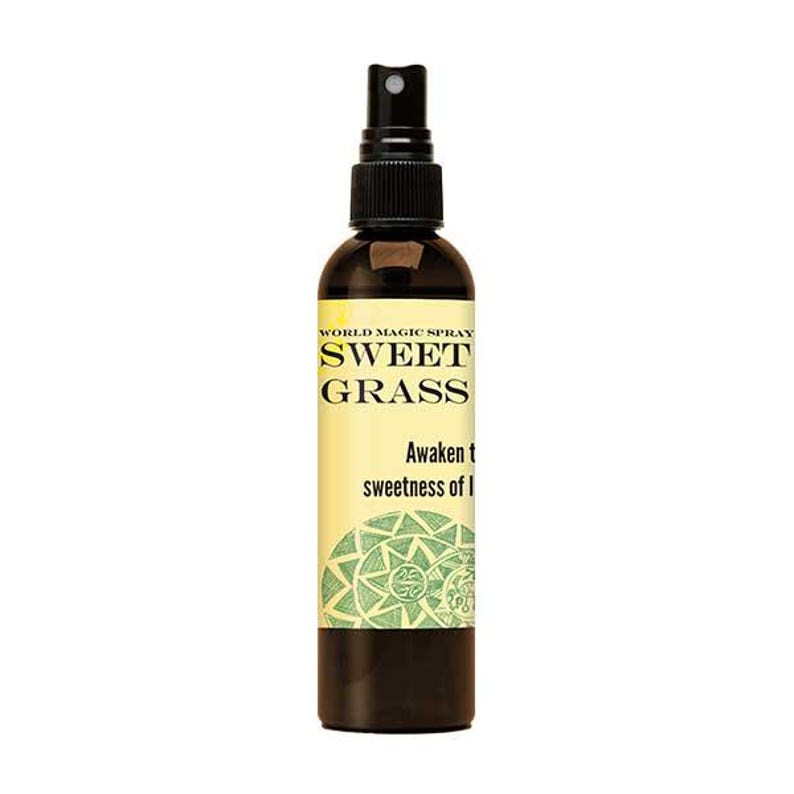 Op de afbeelding: Een bruine glazen spuitfles met een zwarte spuitmond. Het etiket leest "WORLD MAGIC SPRAY SWEET GRASS" met tekst eronder die zegt "Awaken the sweetness of I". Een groen en wit cirkelvormig ontwerp staat onderaan het etiket.
