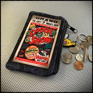 May include: A black zippered pouch with a vintage comic book design featuring a spooky monster and the text "Spook Show". The pouch is lying on a black and white patterned surface.