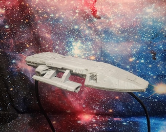 May include: A light gray model spaceship, featuring detailed paneling and a multi-sectioned design. The model is mounted on a black stand, set against a backdrop of a colorful nebula with red, blue, and white hues.