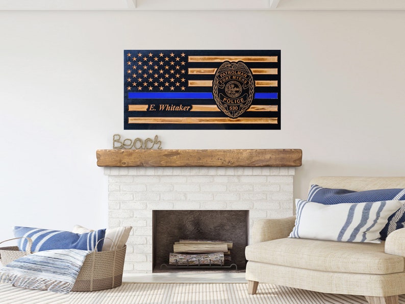 May include: Wooden American flag with a blue line and a police badge with the text "Patrolman Fort Myers Police 530" and the name "E. Whitaker" below the blue line.