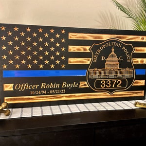 May include: A wooden American flag with a blue line, a Metropolitan Police Department badge, and the text "Officer Robin Boyle 10/24/94 - 05/21/22" and the badge number "3372".