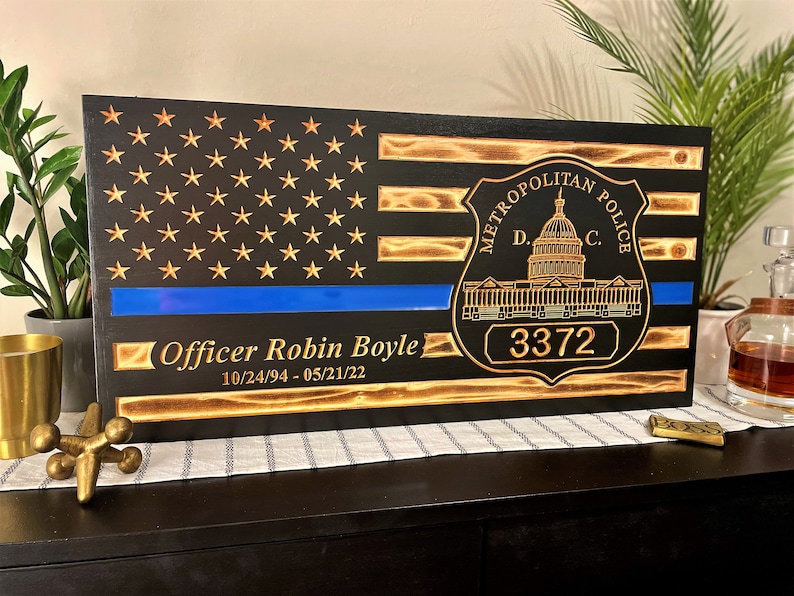 May include: A wooden American flag with a blue line, a Metropolitan Police Department badge, and the text "Officer Robin Boyle 10/24/94 - 05/21/22" and the badge number "3372".