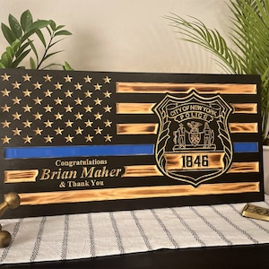 May include: A wooden American flag with a blue line and the New York City Police Department badge. The text "Congratulations Brian Maher & Thank You" is engraved below the flag.