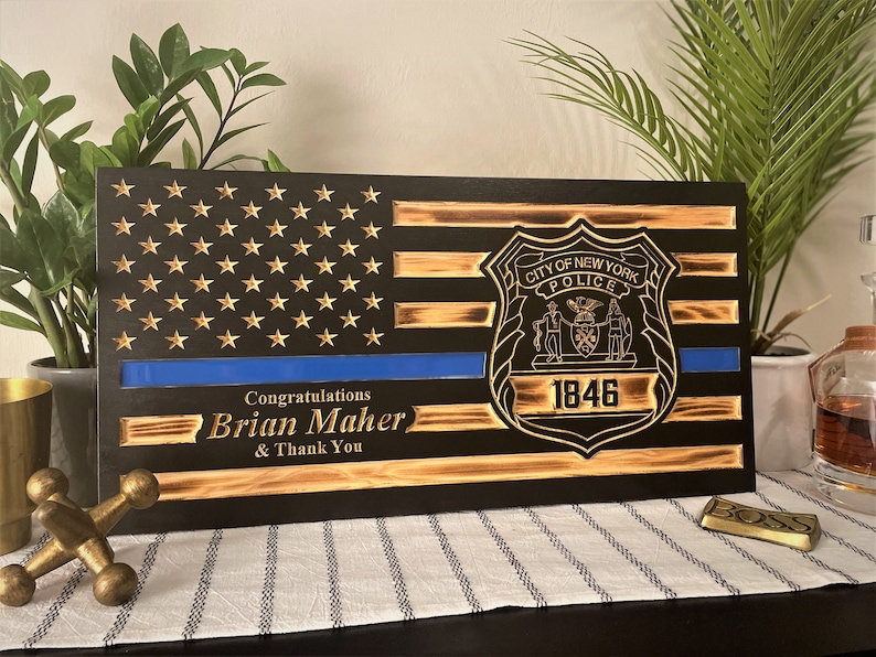 May include: A wooden American flag with a blue line and the New York City Police Department badge. The text "Congratulations Brian Maher & Thank You" is engraved below the flag.