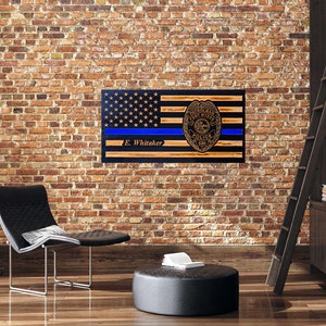 May include: A wooden American flag with a blue line and a police badge. The flag is mounted on a wall and has the name "E. Whitaker" inscribed on it.