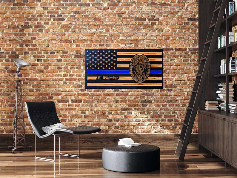 May include: A wooden American flag with a blue line and a police badge. The flag is mounted on a wall and has the name "E. Whitaker" inscribed on it.