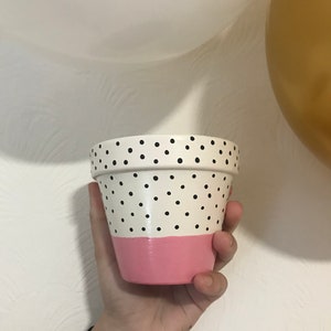 May include: A white terracotta pot with black polka dots and a pink band around the top.