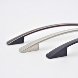 May include: Three cabinet pulls in different finishes: black, brushed nickel, and copper. The pulls are all arched and have a modern design.