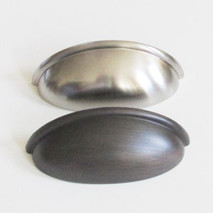 May include: Two cabinet pulls, one in brushed nickel and one in oil rubbed bronze. Both pulls are oval shaped with a slight curve at the top and bottom.