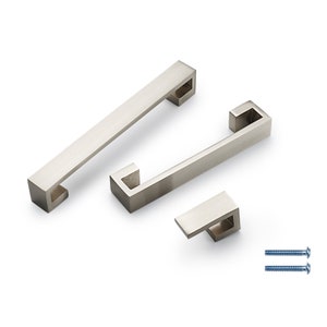 May include: Three brushed nickel cabinet pulls in different sizes. The pulls have a square shape with a rectangular opening. The pulls are shown on a white background.